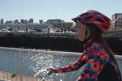 Person biking along waterfront with boats in the background.