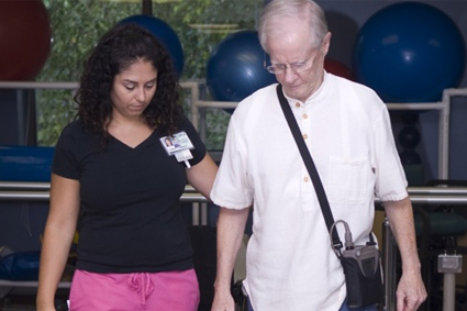 A female caregiver assisting an older man as he walks