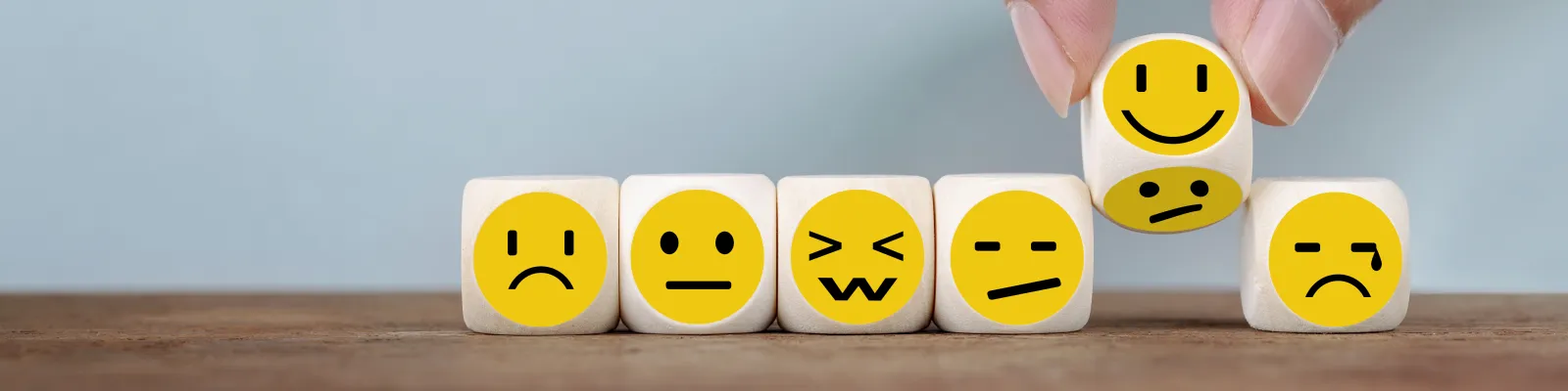 Photo of faces on blocks with different emotions and someone turning the smile over