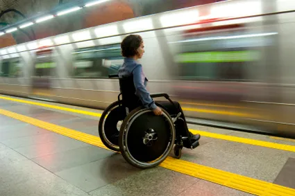 Person in a wheelchair in a subway station as a train rushes past
