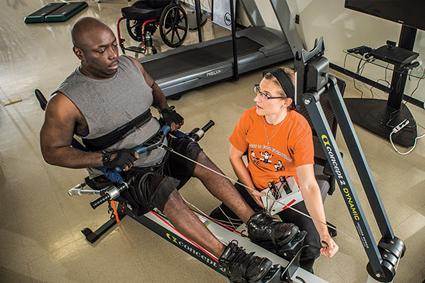 A person with a spinal cord injury using an exercise machine with a trainer