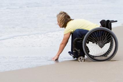 Person in a wheelchair on the beach, leaning down to touch the water
