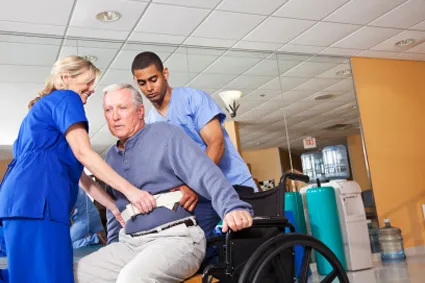 Two nurses helping a man out of a wheelchair