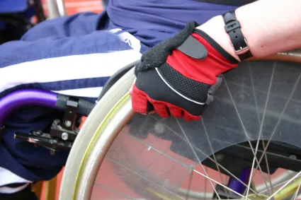 A person sitting in a wheelchair, grasping the wheel with a gloved hand