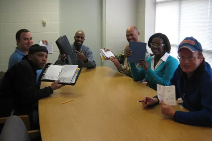 A group of people with notebooks gathered around a conference table 