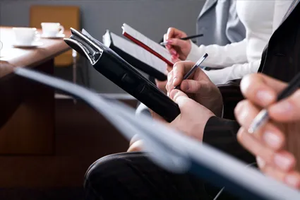 Several people sitting in a row, writing notes on clipboards