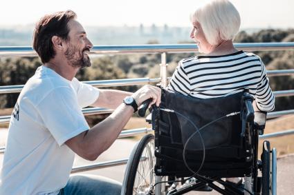 A smiling young man crouching next to an older woman in a wheelchair