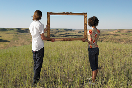 Two people holding a large picture frame showing the distant landscape