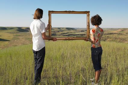People holding empty picture frame in a field