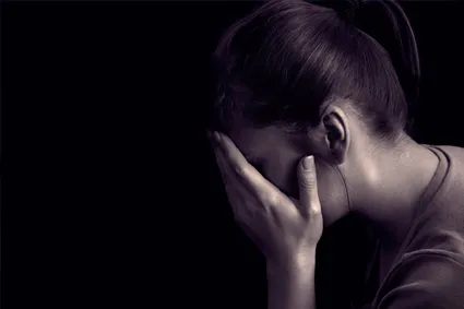 Person in dark room covering face