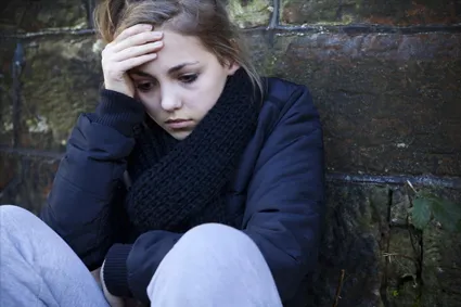 Person leaning against a wall looking upset