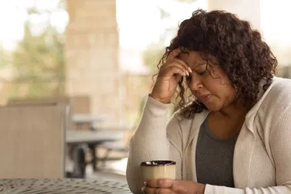 Woman resting head on one hand and holding coffee with the other