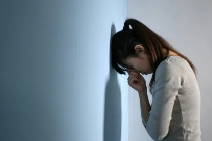 Photo of woman leaning against a wall looking sad