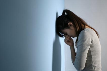 Photo of woman leaning against a wall looking sad