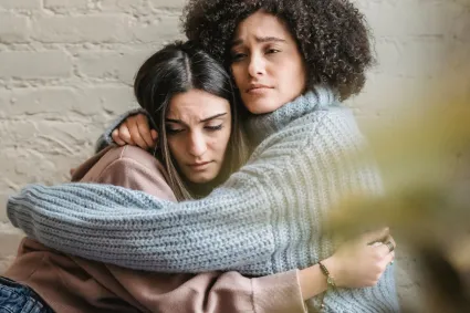 Photo of one person hugging another who looks sad