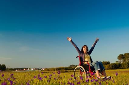 Photo of happy woman in wheelchair in a field with hands in the air