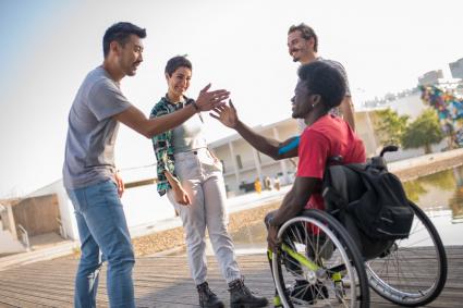 Photo of teen in wheelchair giving high-fives to friends
