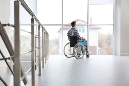 Photo from far away of man in wheelchair looking out a window