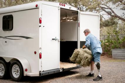 Photo of person with amputated leg putting a straw bale into a trailer