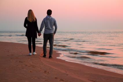 Photo of couple taking a walk on the beach at sunset