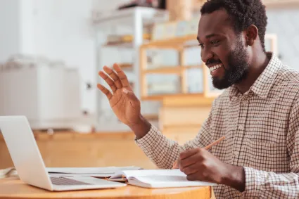 Photo of man at laptop, waving to the screen