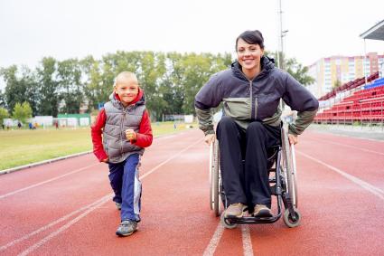 Photo of woman in wheelchair with a little boy walking beside her on a track