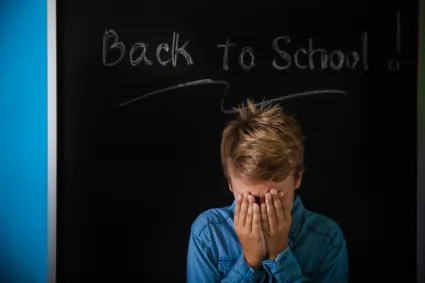 kid holding their head in front of chalkboard
