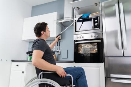 Photo of man in wheelchair reaching a high shelf with an assistive device