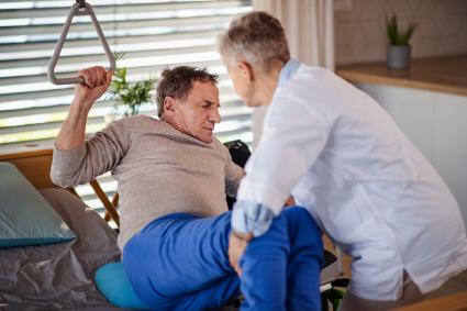 Photo of health care worker helping person move from bed