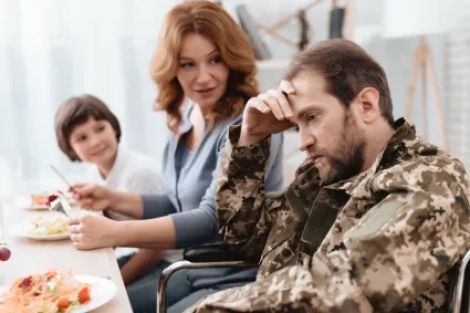 Man in wheelchair looking sad with woman and child looking at him