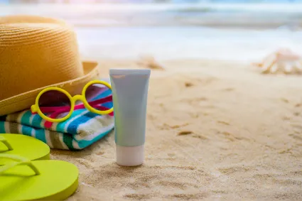 Photo of sunscreen and sunglasses on a beach
