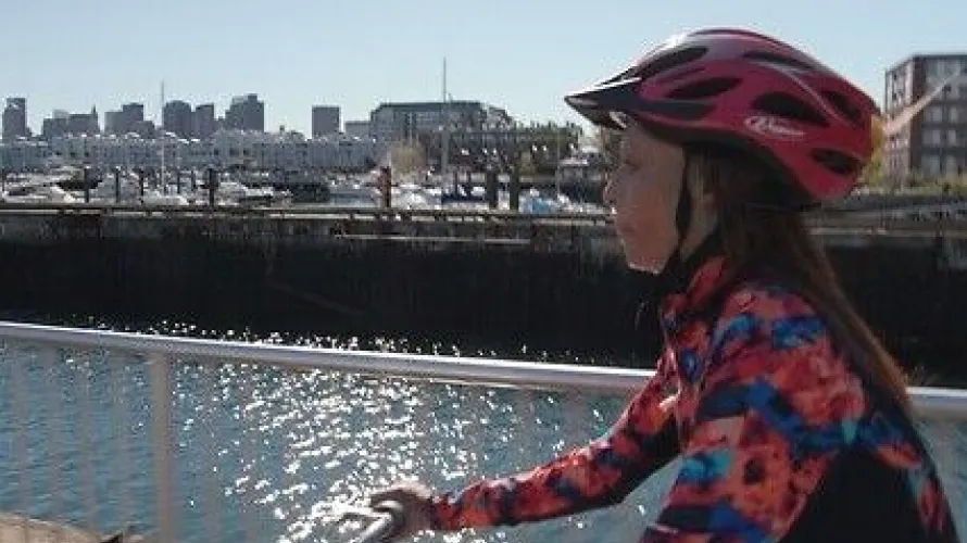 Person biking along waterfront with boats in the background.