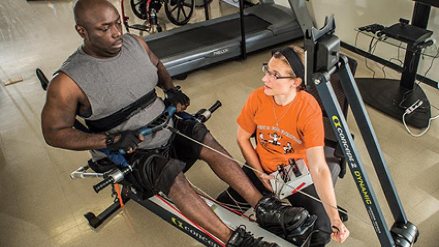 A person with a spinal cord injury using an exercise machine with a trainer