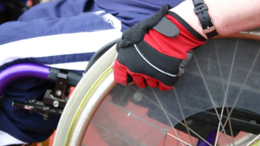 A person sitting in a wheelchair, grasping the wheel with a gloved hand