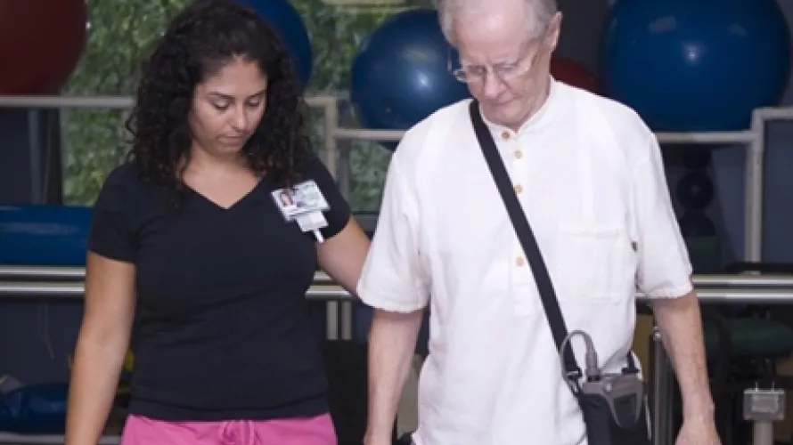 A female caregiver assisting an older man as he walks