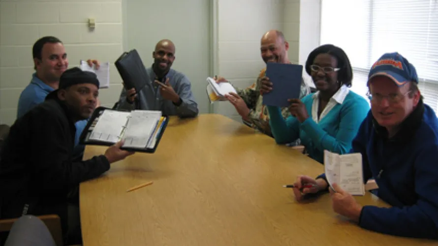 A group of people with notebooks gathered around a conference table 
