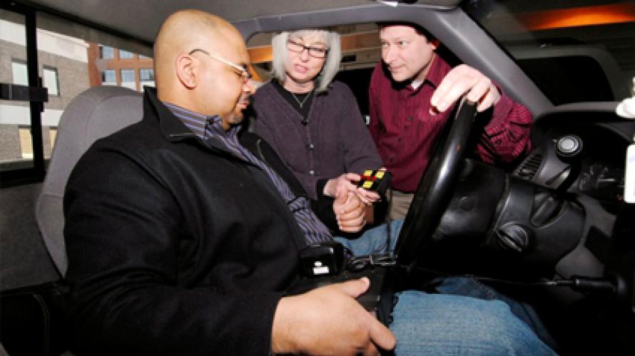 A person sitting in the driver's seat of a car, being instructed by two other people