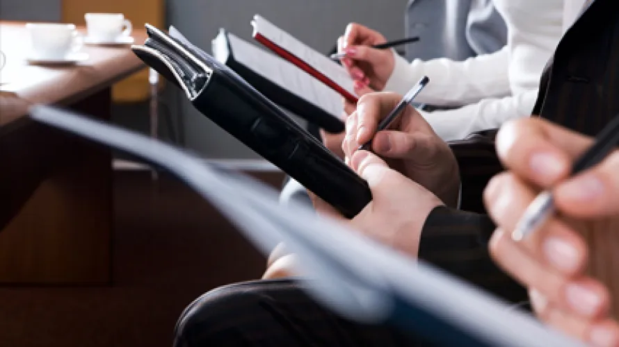 Several people sitting in a row, writing notes on clipboards