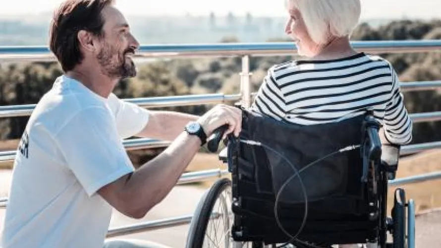 A smiling young man crouching next to an older woman in a wheelchair