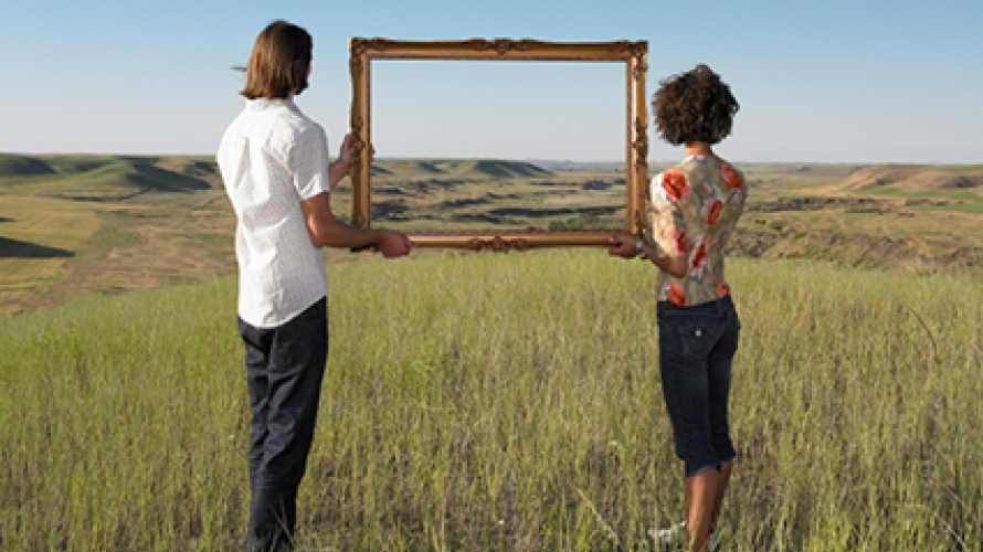 Two people holding a large picture frame showing the distant landscape