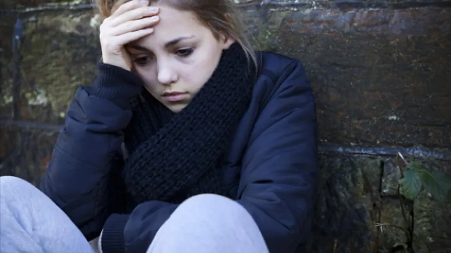 Person leaning against a wall looking upset