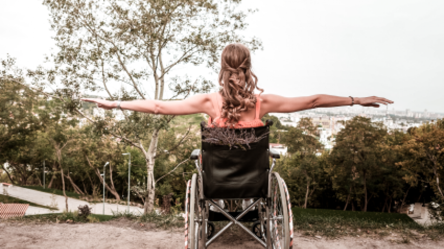 Person sitting in wheelchair looking at view with arms raised out to the sides.
