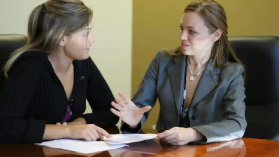 two women sitting at a desk looking at papers